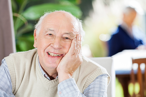 Elderly man with his head resting in his hand smiling